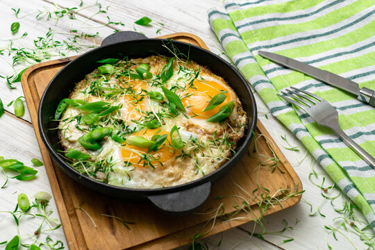 scrambled eggs with greens sprouts and green onions in a pan on a wooden background. - Powered by Adobe
