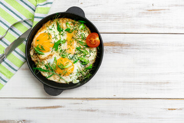 scrambled eggs with greens sprouts and green onions in a pan on a wooden background.