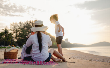 Family, travel, beach, relax, lifestyle, holiday concept. Parents and children who enjoy a picnic at the beach on sunset in holiday.