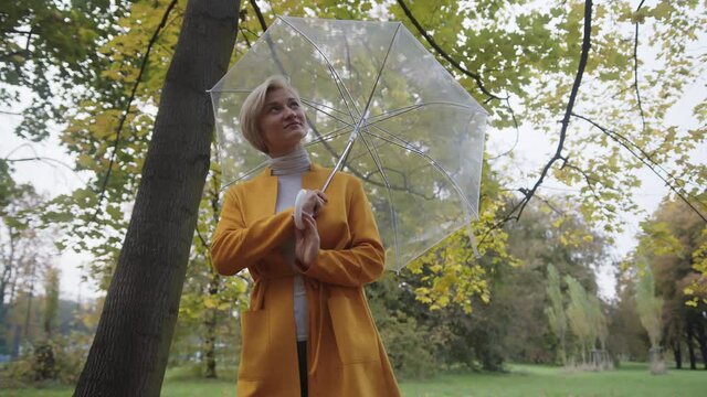 Autumn fashion. Woman with yellow coat and transparent umbrella in the park