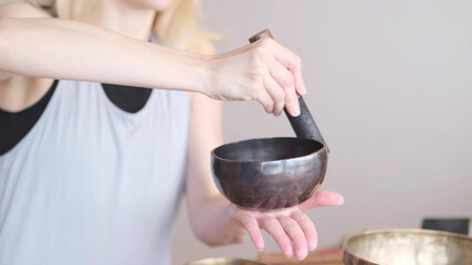 Woman playing on Tibetan singing bowl while sitting on yoga mat. Vintage tonned.