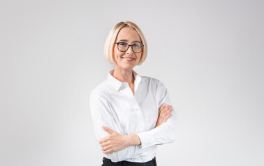 Smiling female entrepreneur in formal clothes and glasses posing with crossed arms on light grey...