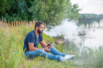 Confident vape man smoking an vape in a forest clearing. Man really likes process of smoking.