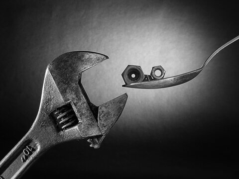 Adjustable wrench with nut and tablespoon on dark abstract background

