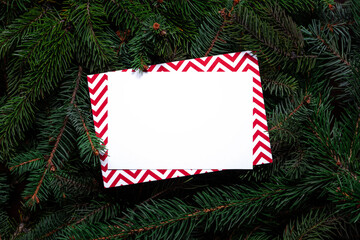 Christmas tree branches with paper card note. Nature New Year concept. Merry Christmas card, background. Congratulations, holidays, celebration. Mock up, copy space, flat lay. Red, green and white.