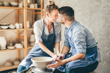 Couple in love working together on potter wheel in craft studio workshop.