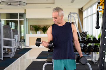 Mature handsome Persian man exercising with dumbbells at the gym