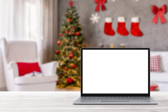 Blank display screen laptop computer on white wood table. Modern cozy comfortable home living room with Christmas decor. Home office desk workspace. Mock up copy space. Winter sales, online shopping