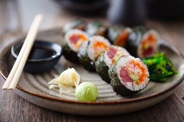 Sushi maki rolls with tuna, flying fish caviar, crab, avocado on a plate with chopsticks, soy sauce, wasabi and ginger. Japanese traditional food closeup served for lunch in modern gourmet restaurant