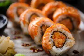 Baked sushi maki rolls with salmon, crab and spicy sauce on a plate with chopsticks, soy sauce, wasabi and ginger. Japanese traditional fish food closeup served for lunch in modern gourmet restaurant