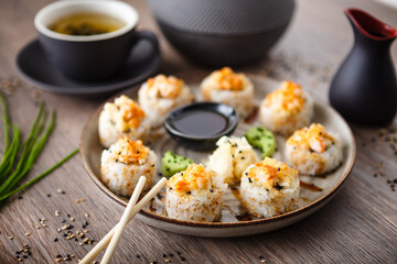 Baked sushi maki rolls with prawns and crab on a plate with chopsticks, soy sauce, wasabi and ginger. Japanese traditional fish food closeup served for lunch in modern gourmet restaurant