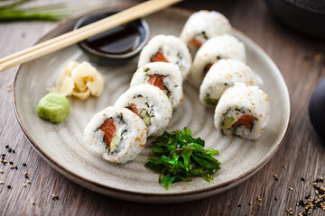 Sushi maki rolls Philadelphia with salmon, creamy cheese and avocado on a plate with chopsticks, soy sauce, wasabi and ginger. Japanese traditional seafood served for lunch in modern restaurant