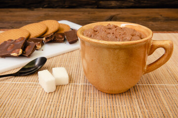 Taza de chocolate caliente, terrones de azúcar junto a una cuchara negra, galletas y chocolate en una bandeja blanca