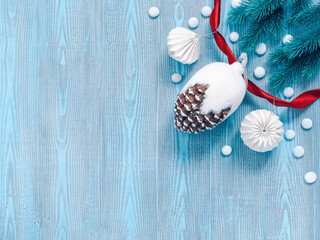 Christmas composition. A large decorative pine cone and paper decorations are on a blue wooden background. Coniferous branches and a red ribbon are nearby. Flat lay, top view, copy space.