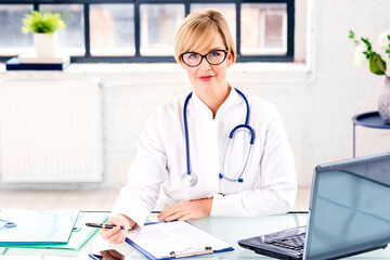 Smiling female doctor sitting at desk and doing some paperwork