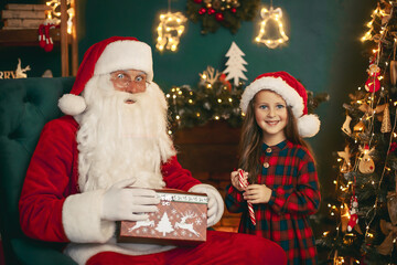 Fototapeta na wymiar Santa Claus with a little cute girl open magical gift box in the room and get candy. Christmas time.