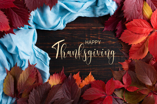 Thanksgiving greetings. Dry red leaves and scarf, on wooden background, top view. Kaligraphic capital inscription.