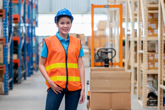 Portrait of warehouse woman or factory worker with blue hat and uniform stand in front of hand stacker or hydraulic cart in workplace. Concept of good management and in delivery industrial business. - Powered by Adobe