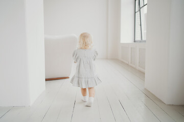 plays at home runs. bright and stylish interior of the apartment. little daughter is a blonde Caucasian girl in a stylish beige dress.