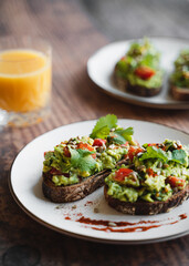 Two avocado toasts on white plate and glass of orange juice