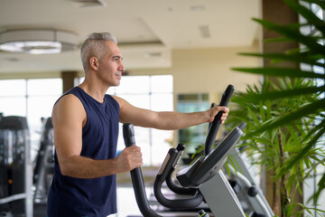 Mature Persian man exercising with elliptical trainer machine at the gym