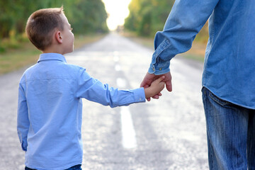 parent holding the hand of a  child walking along the road