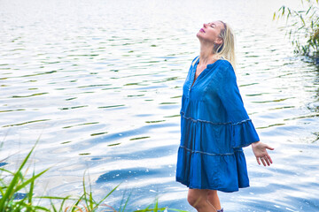 blond woman in blue dress standing in water with rubber boots