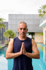 Mature Persian man meditating at the swimming pool on rooftop