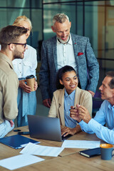 Cheerful multiracial business team using laptop, discussing project results and smiling while having a meeting in the modern office, working together