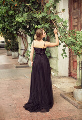 Obraz na płótnie Canvas A girl in a long black dress walks through the old city