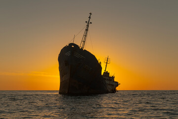 sunset over the sea with a shipwrek in the shadows