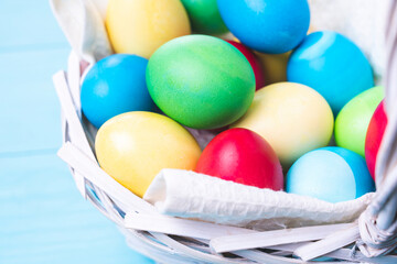 basket with colorful Easter eggs on a blue wooden background, selective focus, tinted image
