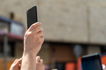 phone in hand holds over the crowd to take photos