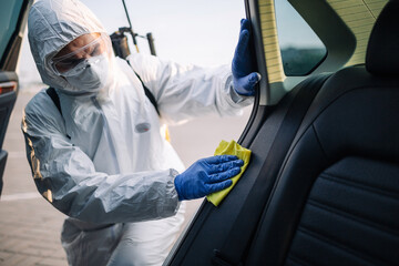 Sanitizing service worker cleans the car's interior with a yellow rug. A man in a protective suit,...