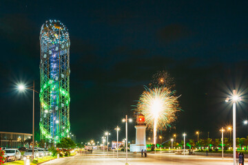 Batumi, Adjara, Georgia. Illuminated Alphabet Tower And Pitsunda Lighthouse At Promenade Near Miracle Park, Amusement City Park On Blue Evening Sky Background. Modern Urban Architecture