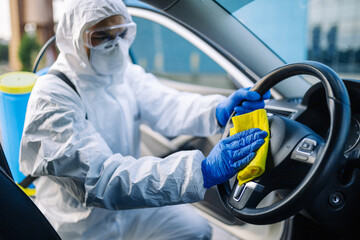 Disinfection professional cleans up a steering wheel of a car with a yellow rug. Sanitary service...