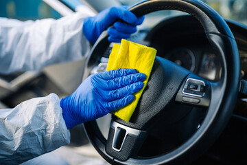 Disinfection professional cleans up a steering wheel of a car with a yellow rug. Sanitary service...