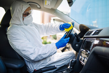 Disinfection professional cleans up a steering wheel of a car with a yellow rug. Sanitary service...