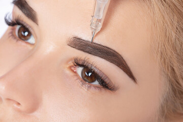 Permanent make-up for eyebrows of beautiful blonde woman in beauty salon. Closeup beautician doing...