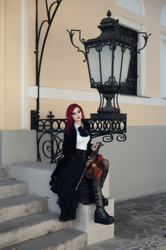 red haired vampire girl plays the violin in an old Museum in Gothic black clothes and a tailcoat