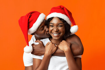 Obraz premium Romantic black guy in Santa hat hugging and kissing girlfriend