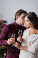 passionate couple holding glasses with champagne near christmas tree on blurred background
