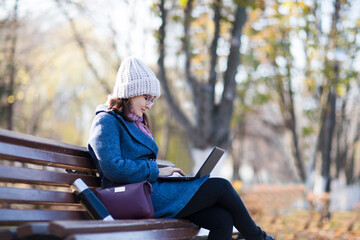 Happy  young woman working on laptop  in autumn at city park. 
