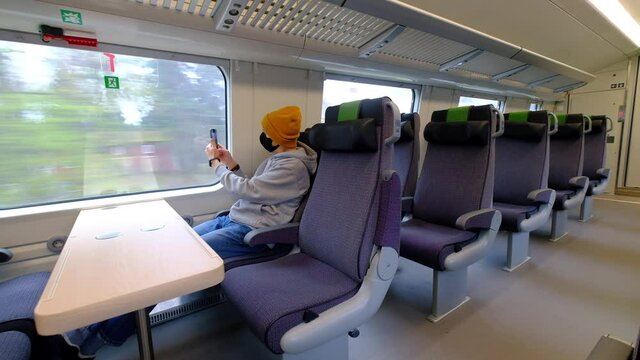 A man in a black protective mask sits alone in the train and he is taking the picture with the smartphone.