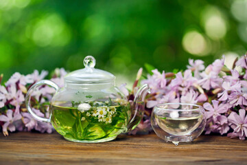 Obraz na płótnie Canvas Herbal tea in a glass cup and teapot with bouquet of pink flowers on a green bokeh background. Summer tea ceremony in a garden.