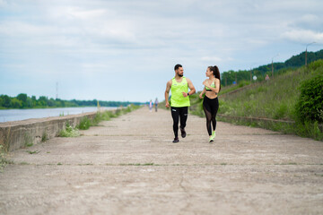 Running young couple in stylish sportswear outdoor in cloudy weather, healthy active lifestyle