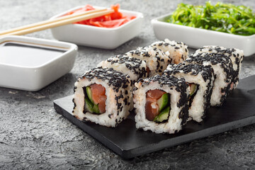Sushi with salmon on a dark background. Sushi with Chuka salad, ginger and soy sauce.