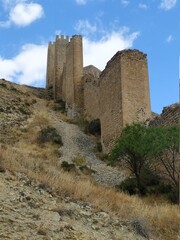 Fototapeta na wymiar Muralla de castillo en ruinas en ladera de montaña con cielo azul