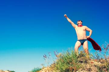A brutal man wearing swimming trunks posing on the beach imitating a flying superhero. Copy space