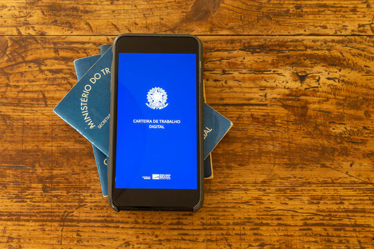 Rio de Janeiro, Brazil - October 19, 2019: a digital working Brazilian working permit, the CTPS, with the traditional paper document on a wooden table